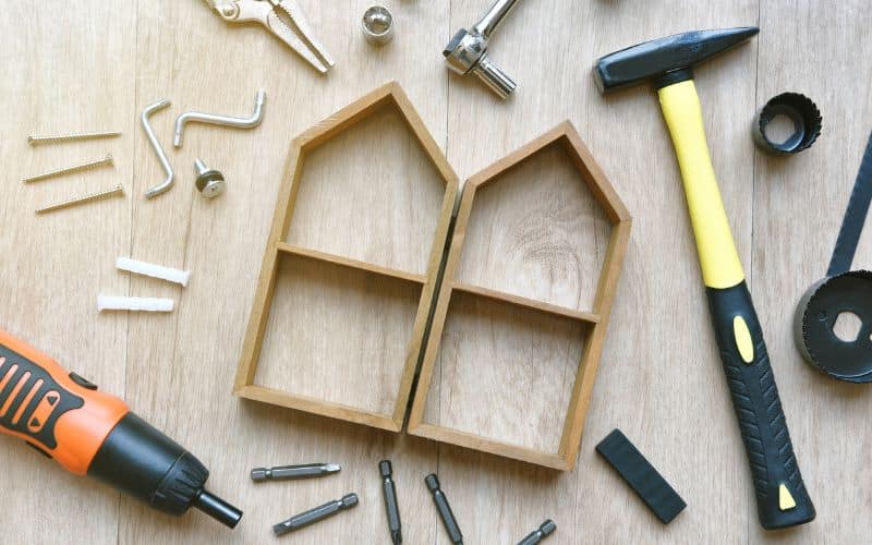 An outline of a house made from lengths of wood set out on a table and surrounded by tools used in the maintenance of bamboo homes.