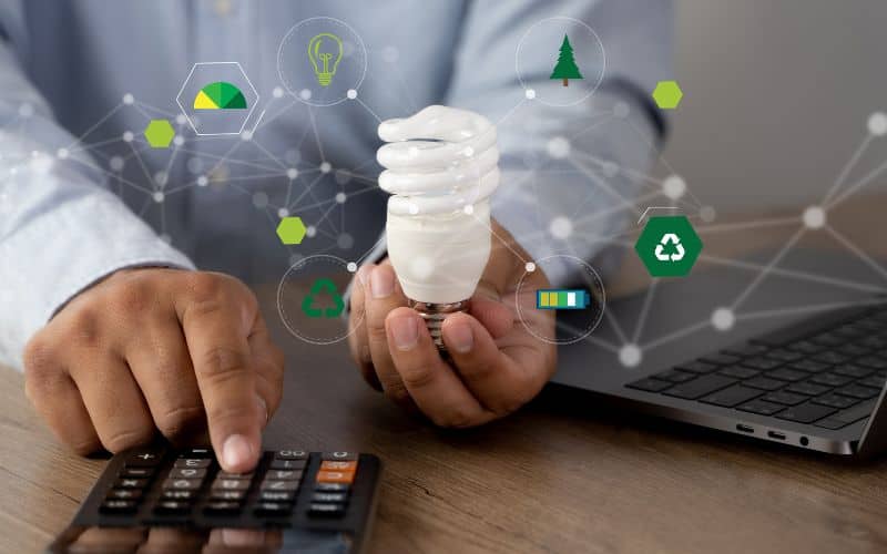 A man holding an energy-saving light bulb and working out his energy savings on a calculator.