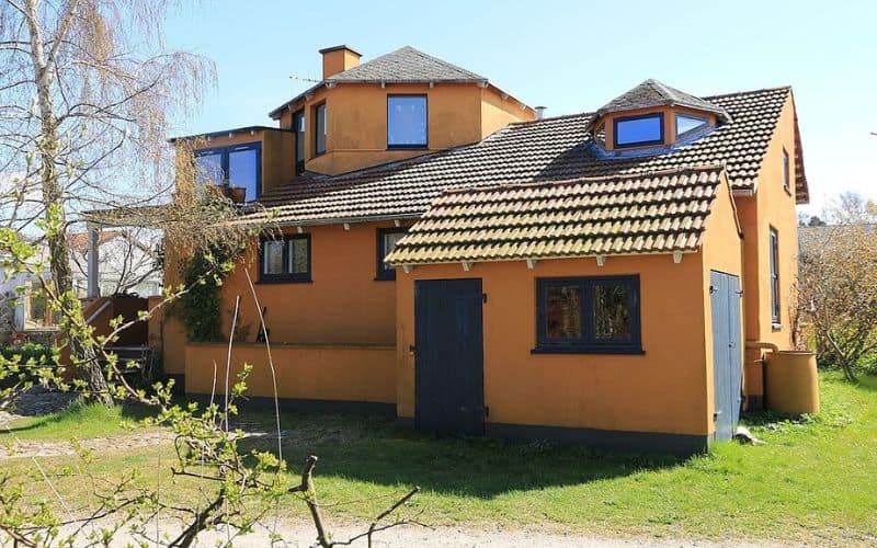 A straw bale house in a country style with orange walls and dormer windows.