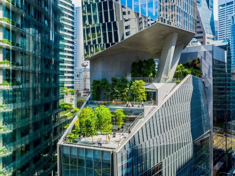 An image of 18 Robinson Tower in Singapore. The building is sheer glass all the way around the outside but with an open air section "cut away" part way up. the cut away provides an outdoor area for people to use and is terraced with trees an balconies on it. It is surrounded by other tall buildings.