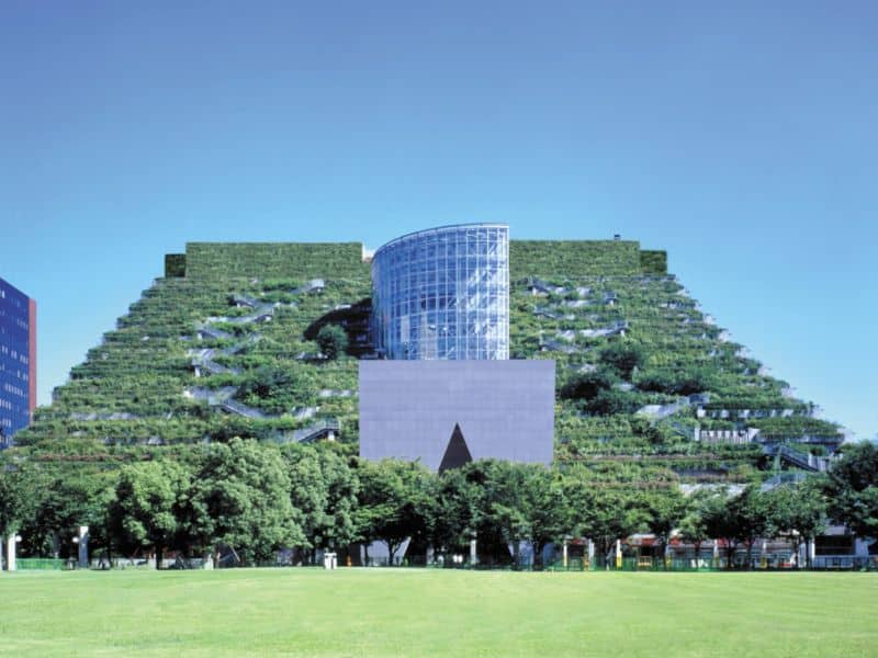 An image of the ACROS Fukuoka Prefectural International Hall in Fukuoka, Japan. It is trapezoidal in shape with a central turret that is full of windows. The rest of the building appears to be covered in shrubbery, like a natural hillside.