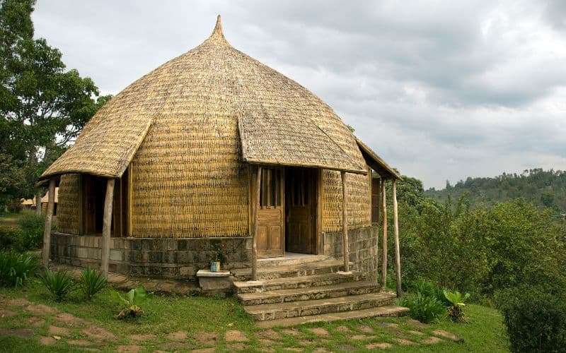 A single-storey bamboo house. The house is round in plan and has a domed roof. There are steps leading up from the ground and the house appears to be built on a slightly elevated concrete block foundation.