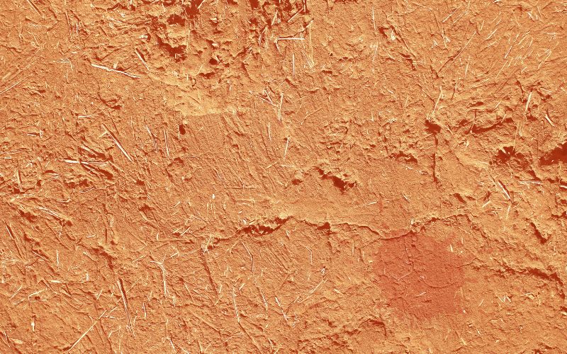 A clay plaster wall. The clay is red and there are small pieces of straw visible.