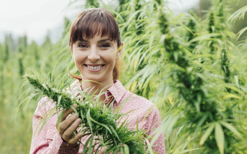 A woman looking happy having found some hemp, which she is holding up to the camera and smiling.