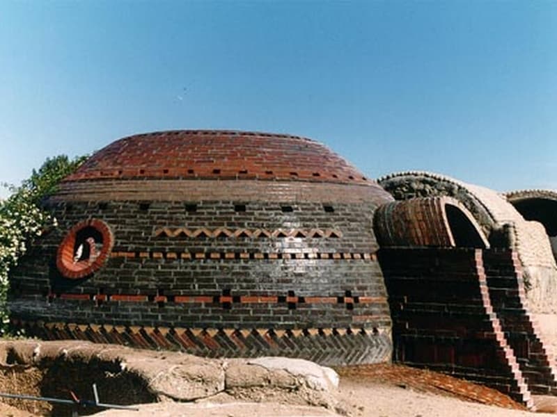 A fired ceramic ‘Geltaftan’ building. It is dome shaped and has patterns in it from different shapes and colors of ceramic brick. There is a circular window in the side.