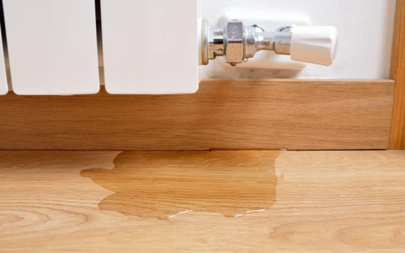 A radiator leaking water onto a hemp wood floor.