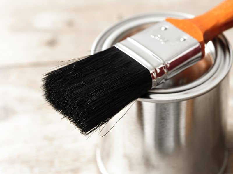 A steel tin of paint with a clean paintbrush lying across it. The paint pot is still sealed.