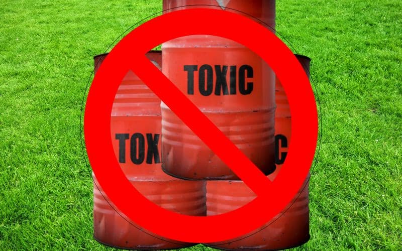 Three red oil drums with the word "toxic" written on each one in black capital letters. There is a "forbidden" sign over the top of them comprising a red circle with a red line diagonally through it. The background of the image is a green lawn.