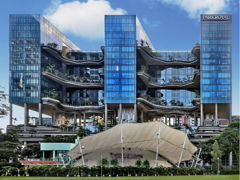 An image of PARKROYAL Collection Pickering in Singapore. This is a building comprising three box-shaped glazed buildings linked by three levels of bridge that has lots of greenery.