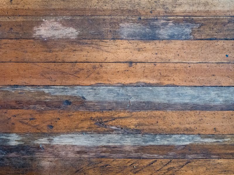 A series of wooden planks that have a distressed appearance due to wear and tear. A few splinters can be seen and the varnish has rubbed off in places.