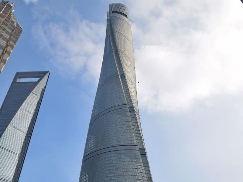 An image of the Shanghai Tower, which stands 632m tall. It has the appearance of a spiral from the outside and is set against the background of a blue sky with white clouds.