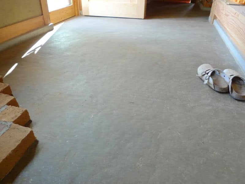 A traditional Japanese Earth Floor. There is a pair of sandals on the edge of the floor, which is pristine and light gray in color.