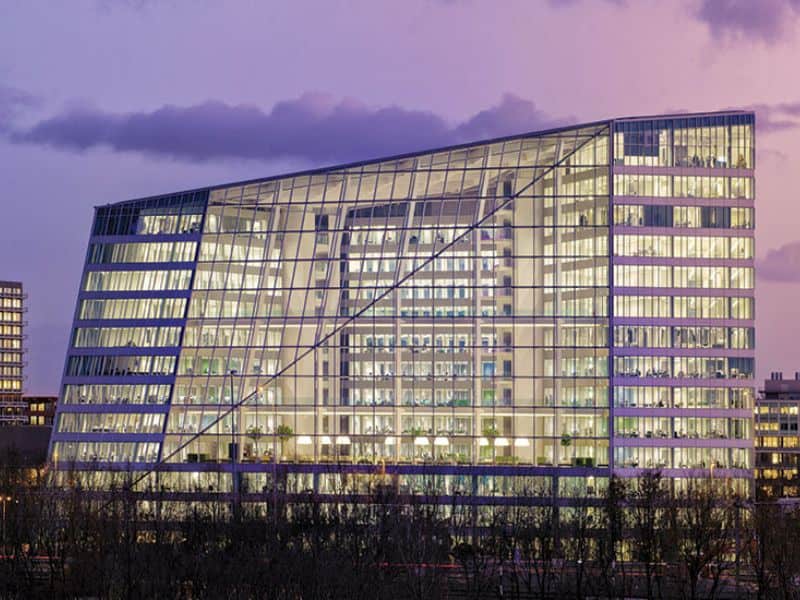 An image of The Edge, Amsterdam, Netherlands. It is an entirely glazed building with little wall surface area that is not glass.The roof slopes from right to left in the image, which is taken at night with the building's interior lit up.