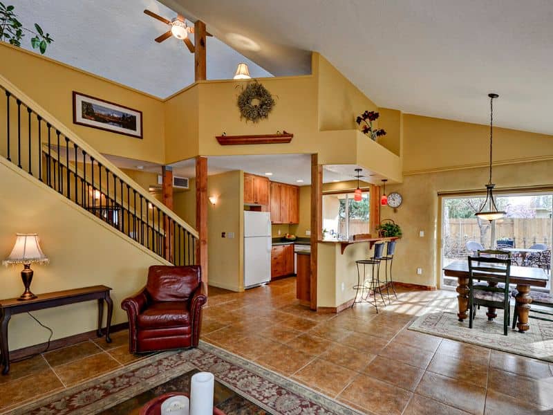 The interior of a Boise Straw Bale home. It is airy and spacious with an orange tiled floor and yellow walls. There is a staircase on the left of the image and a large rug on the floor in the foreground.