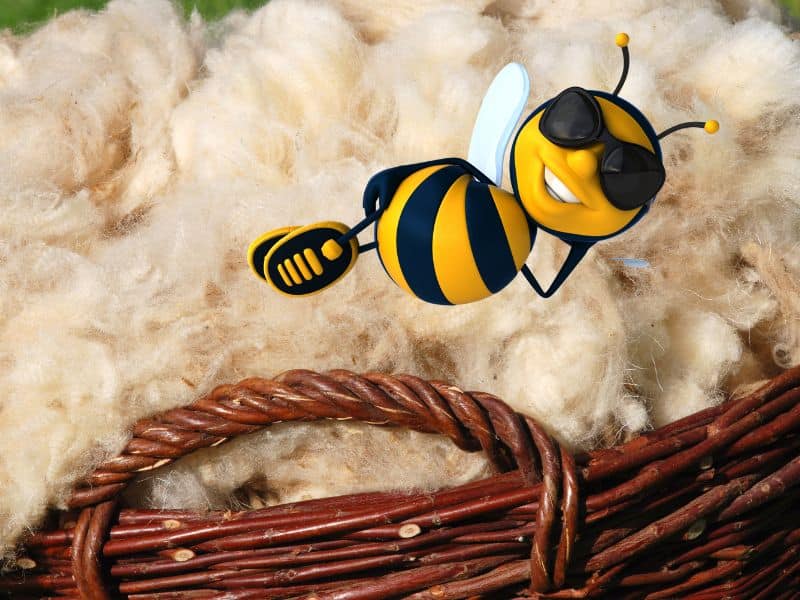 A basket of sheep's wool with a cartoon bee reclining on top of it wearing sunglasses and grinning.