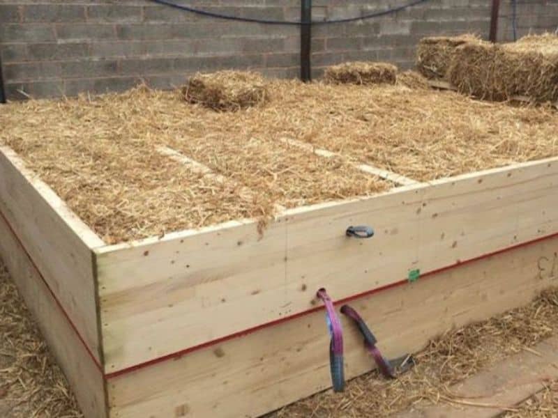 A prefabricated straw bale cassette lying on the ground on top of another cassette. The cassettes are wooden frames packed with straw that can be quickly assembled on site.