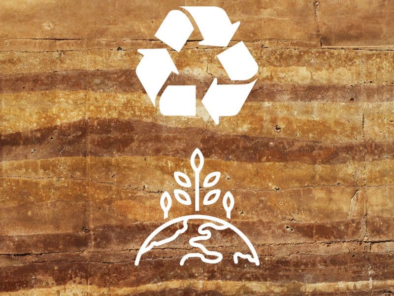 A rammed earth wall with recycling arrows and a cartoon of the earth with plants growing out of it to symbolise sustainability and recyclability.