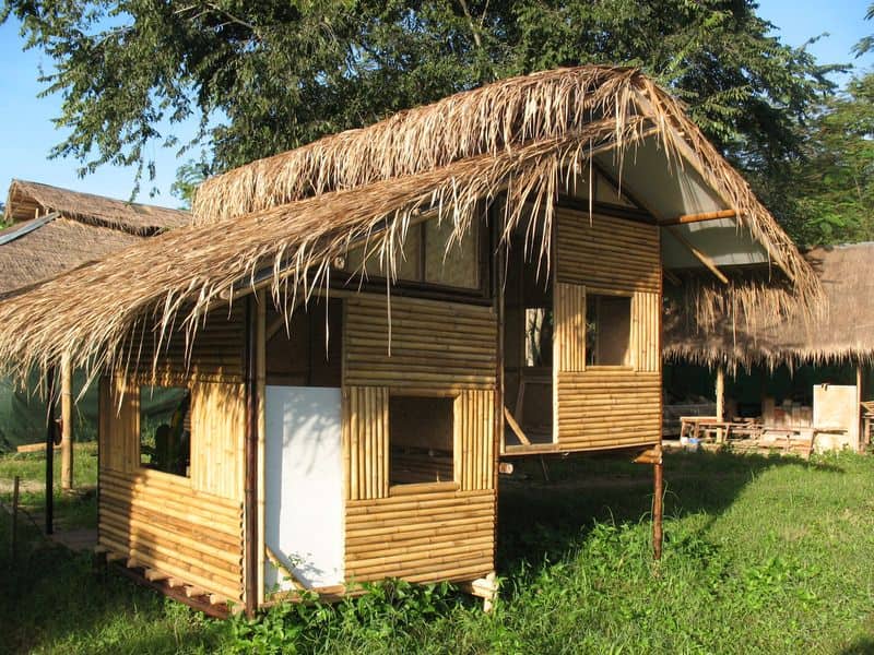 A bamboo house with a thatched roof that overhangs the walls by a long way.