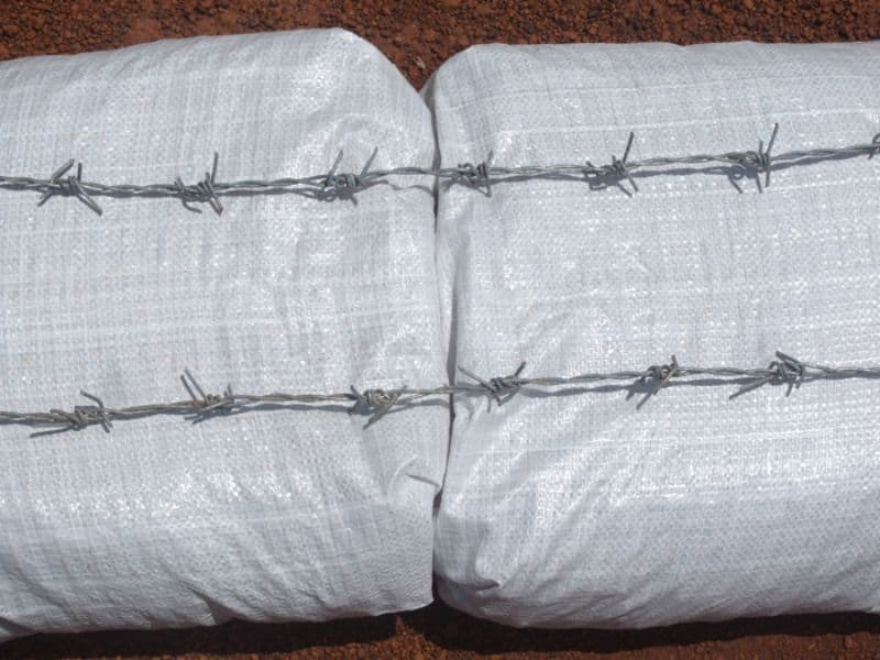 Two straight lengths of barbed wire laid on top of white earthbags.