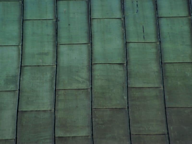 Weathered copper roof tiles over a bamboo roof. The weathering has resulted in a green patina covering the surface of the copper tiles.