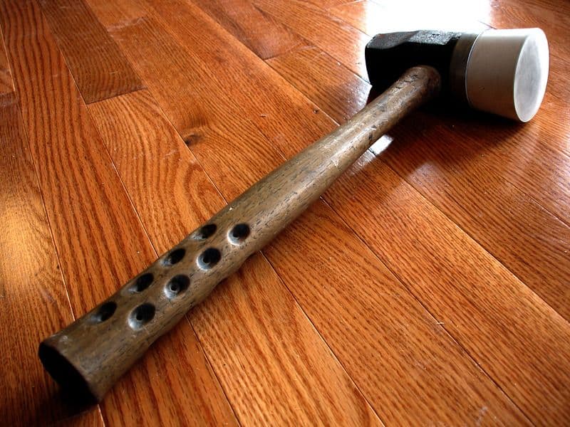 A photograph of a shiny brown engineered hardwood floor with a hammer lying on it.