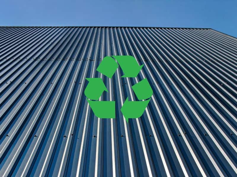 A photograph of aluminum roof panels on a pitched roof. The panels are blue-gray in color and fixed in position using rows of fixing screws. There are three green recycling arrows overlain in the center of the image.