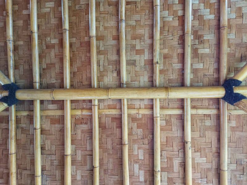 A well-designed and engineered bamboo roof. The ridge is a thick section of bamboo culm lashed with black cord to other main members also made of bamboo. There are thinner cross-pieces arranged perpendicular to the main ridge member at regular intervals. Above this is a woven layer of bamboo strips or "splits".