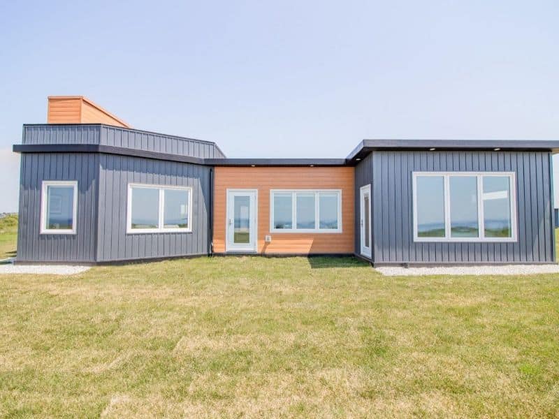 A single story building made from PET foam panels. There are three sections - an orange section in the middle with gray sections either side. There are white framed windows and doors and a lawn outside.