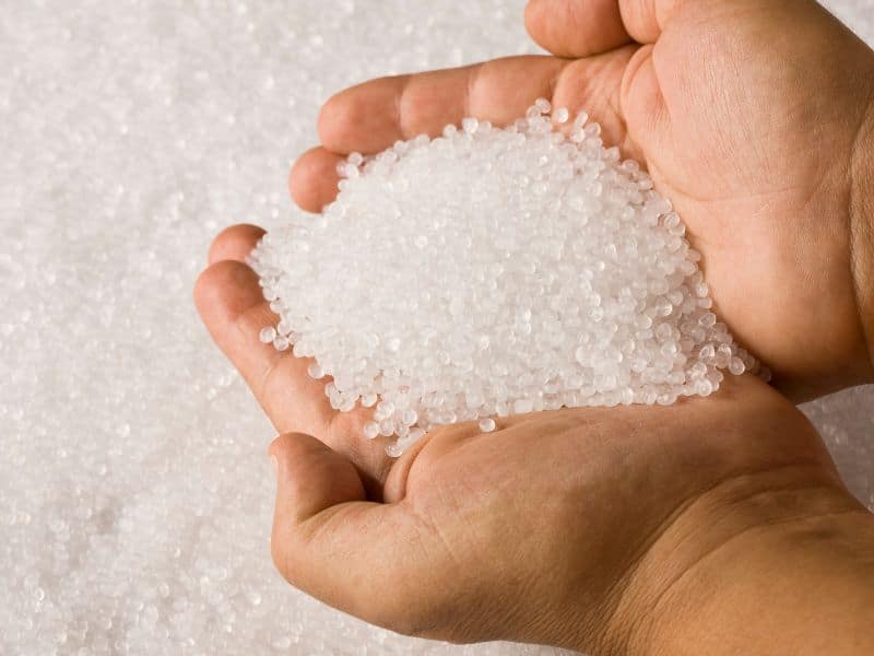 A pair of cupped man's hands holding a pile of small diameter white plastic pellets. Many more of the pellets can be seen below.