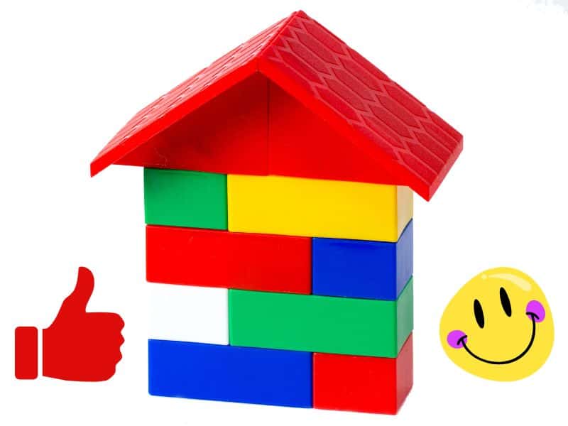 A photograph of a model plastic house built from Lego bricks. The bricks are different colors, which include a red pitched roof and red, green, yellow, blue and white walls. There is a red "thubmbs up" icon to the left of the image and a yellow smiley face on the right.