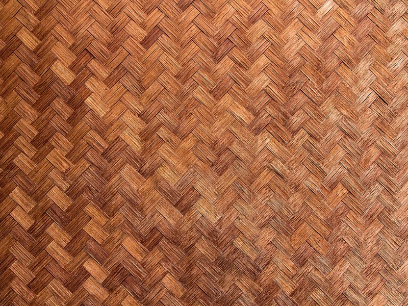 A woven section of brown bamboo sheet roofing material. The individual flat bamboo strips or "splits" form a herringbone pattern thanks to the interlocking weaving.