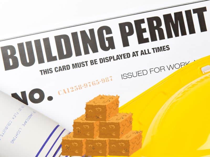 A photo of a building permit with a yellow hardhat resting on top of it. There is an icon of a stack of straw bales overlain.