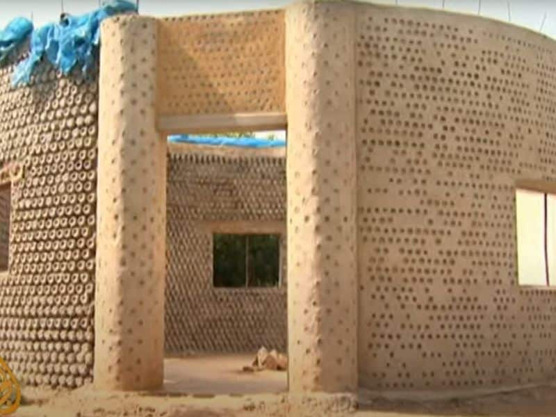 A house in Nigeria built with bricks made from discarded plastic bottles filled with compacted sand. The house is round with rectangular windows. The ends of the individual bottles can be seen in the walls. The walls are held together with string and mud mortar.