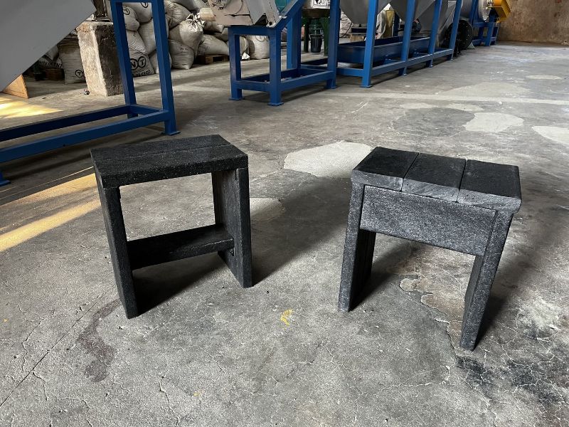 Two stools made from plastic-based eco-lumber by The Plastic Flamingo. The lumber is dark gray or black and has a wood-like texture to it. The stools are sitting on a concrete floor.