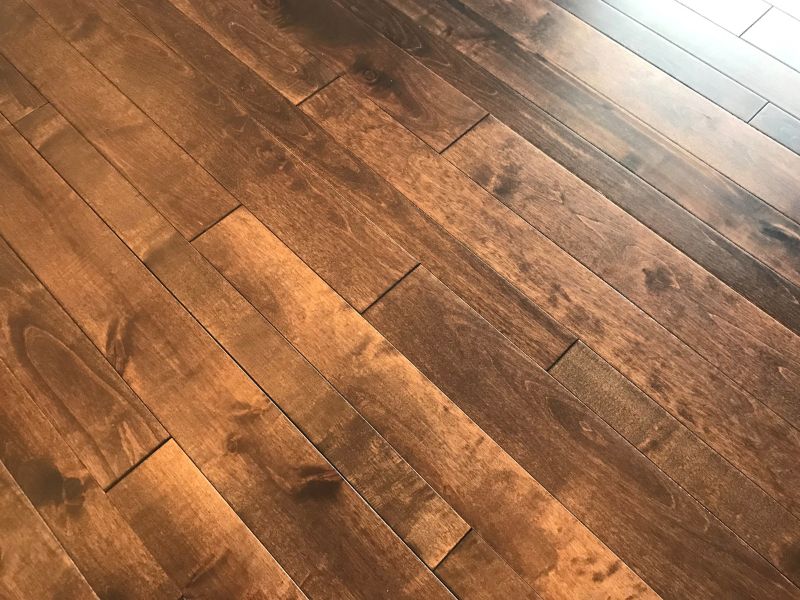 A photograph of a dark brown hardwood floor with individual floorboards of different widths and a beautiful grain pattern. They are highly polished and daylight is being reflected from the boards in the top right corner.