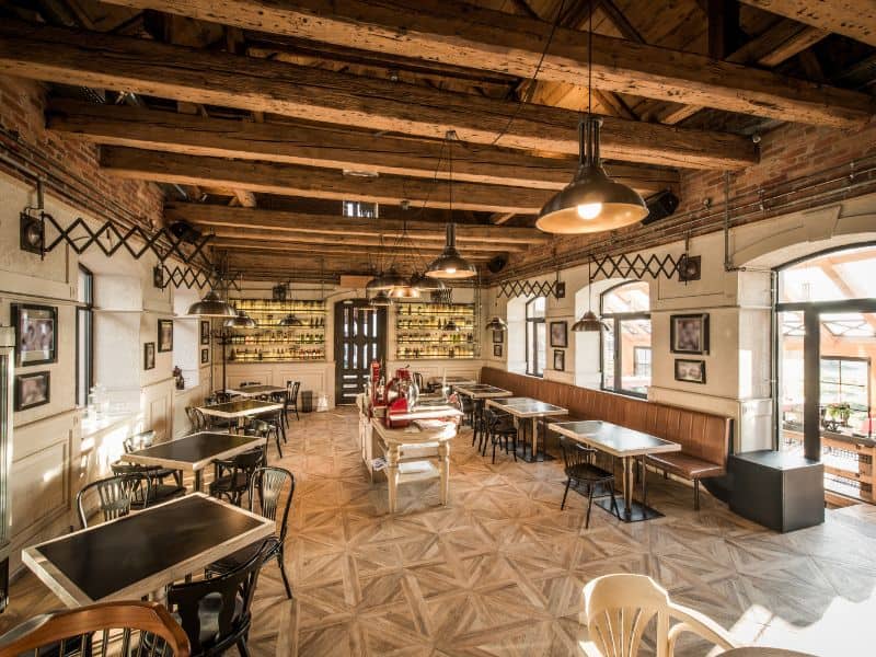 A reclaimed wood vaulted ceiling over a restaurant with tables and chairs arranged across the floor. Electric lights hang down from the beams of the ceiling.