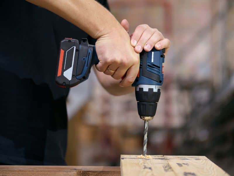 A worker drilling through an LVL beam using a cordless drill.