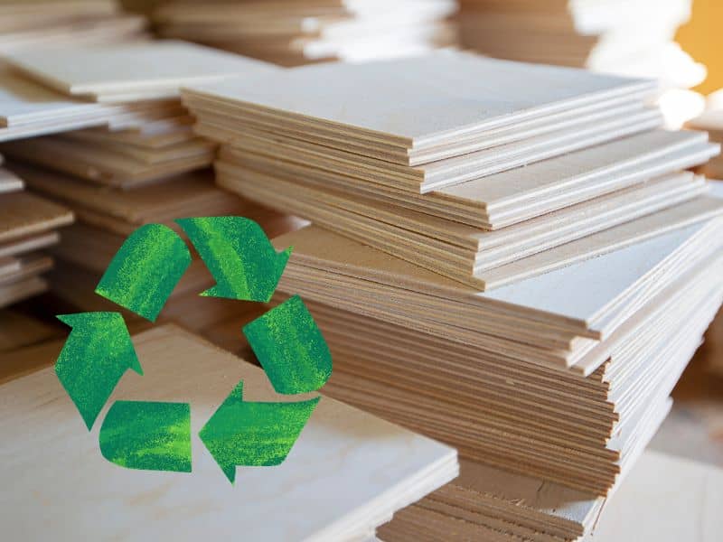 A stack of freshly manufactured plywood with the layers of its component parts visible on its sides. In the bottom left of the photo is a recycling icon in textured green to indicate sustainability.