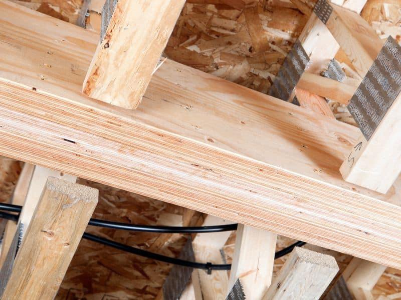 An LVL engineered wood beam supporting a floor in a building. The wooden structure is exposed, and OSB sheathing can be seen beyond.