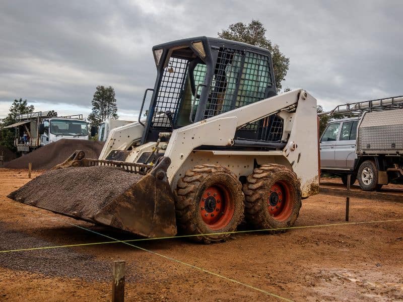 A small earth-moving machine on a building site. The front bucket is full of sand and gravel.