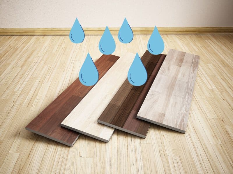 A light brown wood laminate floor with individual planks of alternative colors and designs of laminate flooring arranged in an overlapping pattern on top of it. There are cartoon water droplets overlain above the planks.