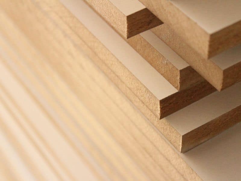 Sheets of Medium-Density Fiberboard (MDF) are stacked haphazardly on top of each other. The sides of the sheets are exposed allowing the dense nature of the tiny particles of wood used in its manufacture to be seen.