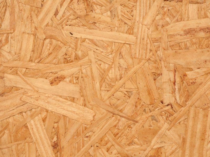 A sheet of light brown oriented strand board (OSB). The board is viewed from above, showing its flat surface with randomly oriented strands of wood fibers.