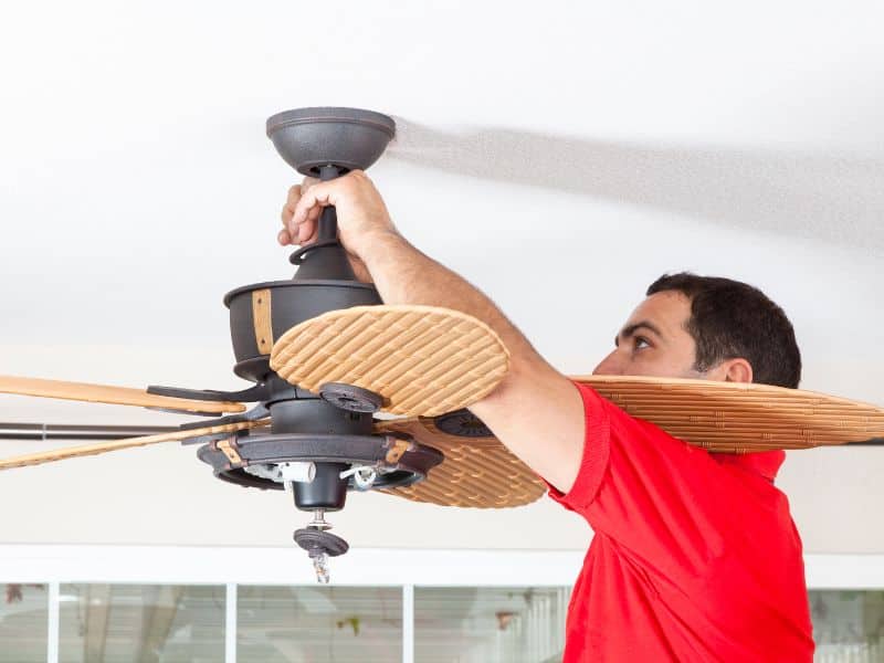 A worker removes a ceiling fan from the ceiling before starting to install reclaimed wood. The worker is a man dressed in a red T-shirt.