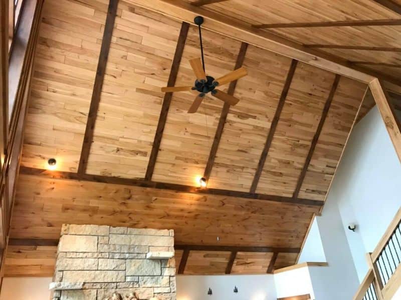 A reclaimed hickory wood ceiling with a vaulted design and wood paneling. A ceiling fan hangs from the central beam and light fittings are installed just above where the walls meet the ceiling.