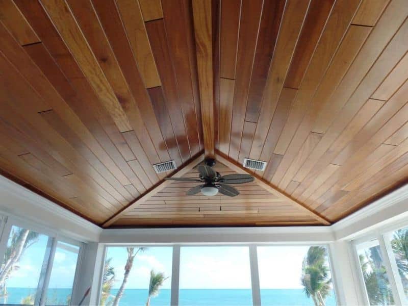 A reclaimed African mahogany ceiling with vents and a ceiling fan. The walls have floor-to-ceiling windows with white window frames.