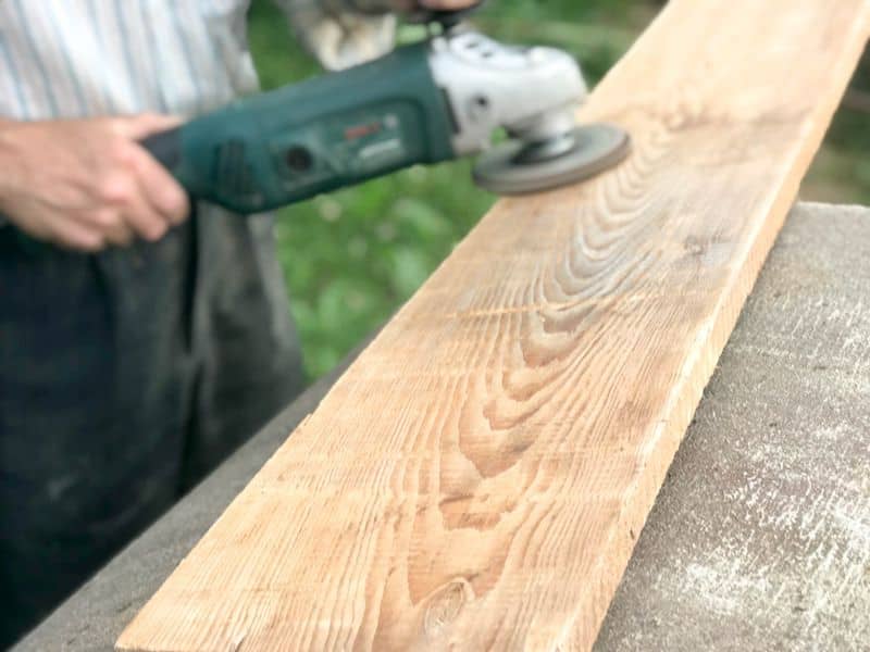 A wooden plank being sanded with a power tool to clean it up and make it smoother.