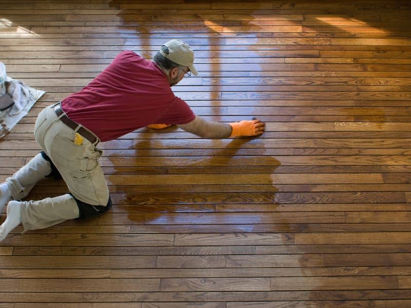 A worker kneeling on a reclaimed wood floor applying natural oil as a finishing to provide protection and improve the durability of the wood.