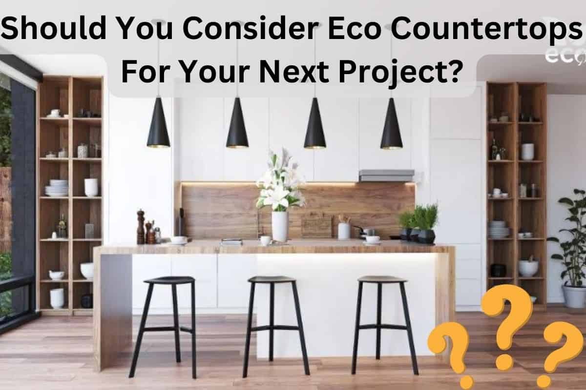 A white kitchen with brown wood eco countertops in a bright open living space. Across the top of the image are the words, "Should You Consider Eco Countertops For Your Next Project?" There are three black stools at the countertop and flowers on top of it.