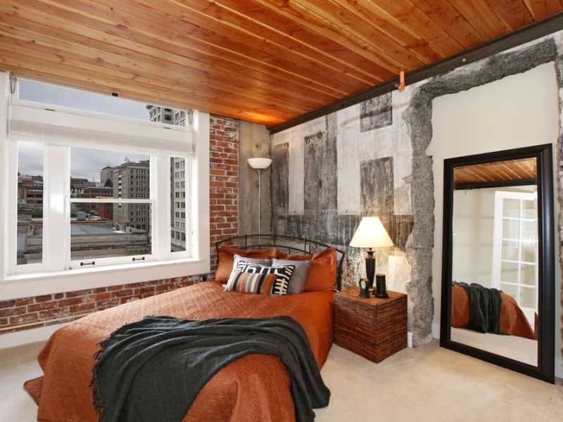 A teak reclaimed wood ceiling in a bedroom with a window overlooking a cityscape. The external wall is bare red brick.